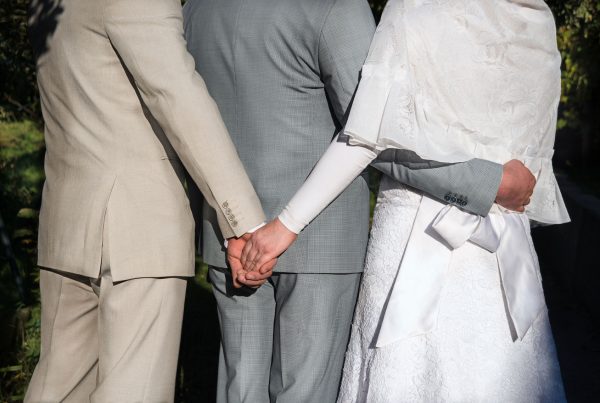 Bigamia – dwie osoby trzymające za ręce jednego partnera podczas ceremonii ślubnej