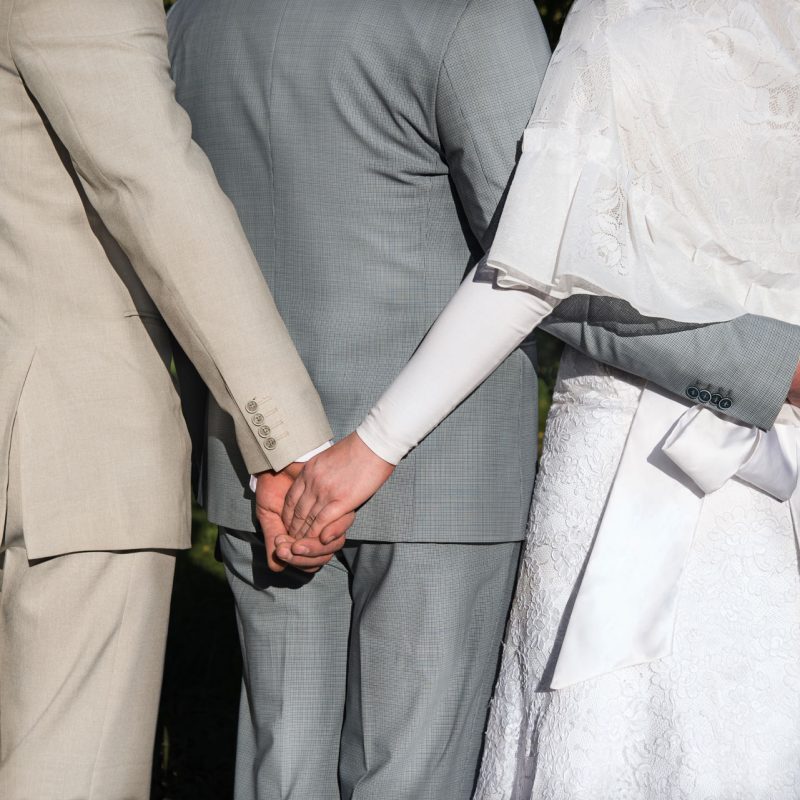 Bigamia – dwie osoby trzymające za ręce jednego partnera podczas ceremonii ślubnej